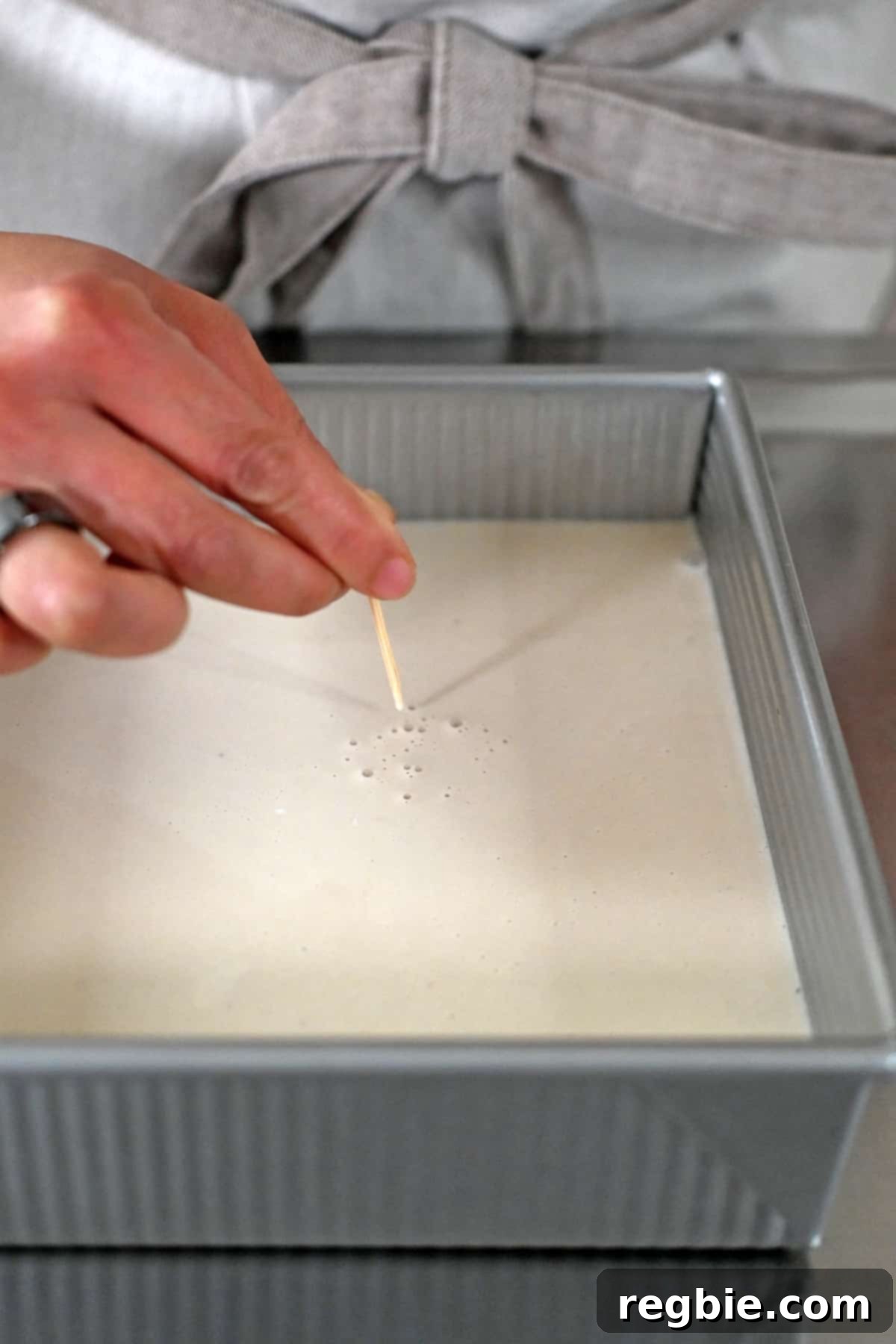 Using a toothpick to carefully pop any air bubbles on the surface of the creamy coconut filling for a grain-free strawberry pretzel salad, ensuring a smooth finish.