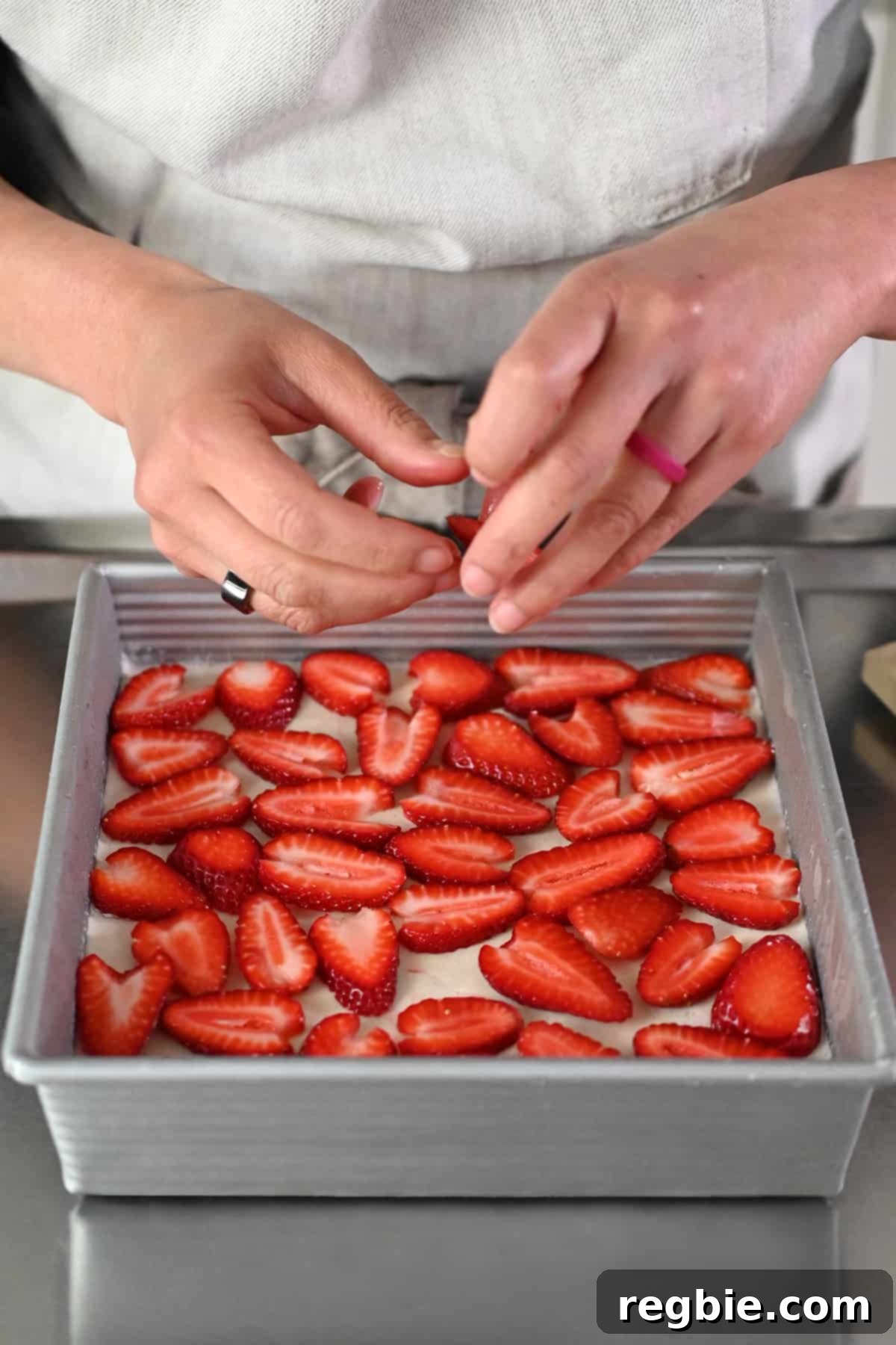 Adding perfectly sliced fresh strawberries in a single layer on top of the solidified grain-free strawberry pretzel salad base, preparing for the gelatin layer.