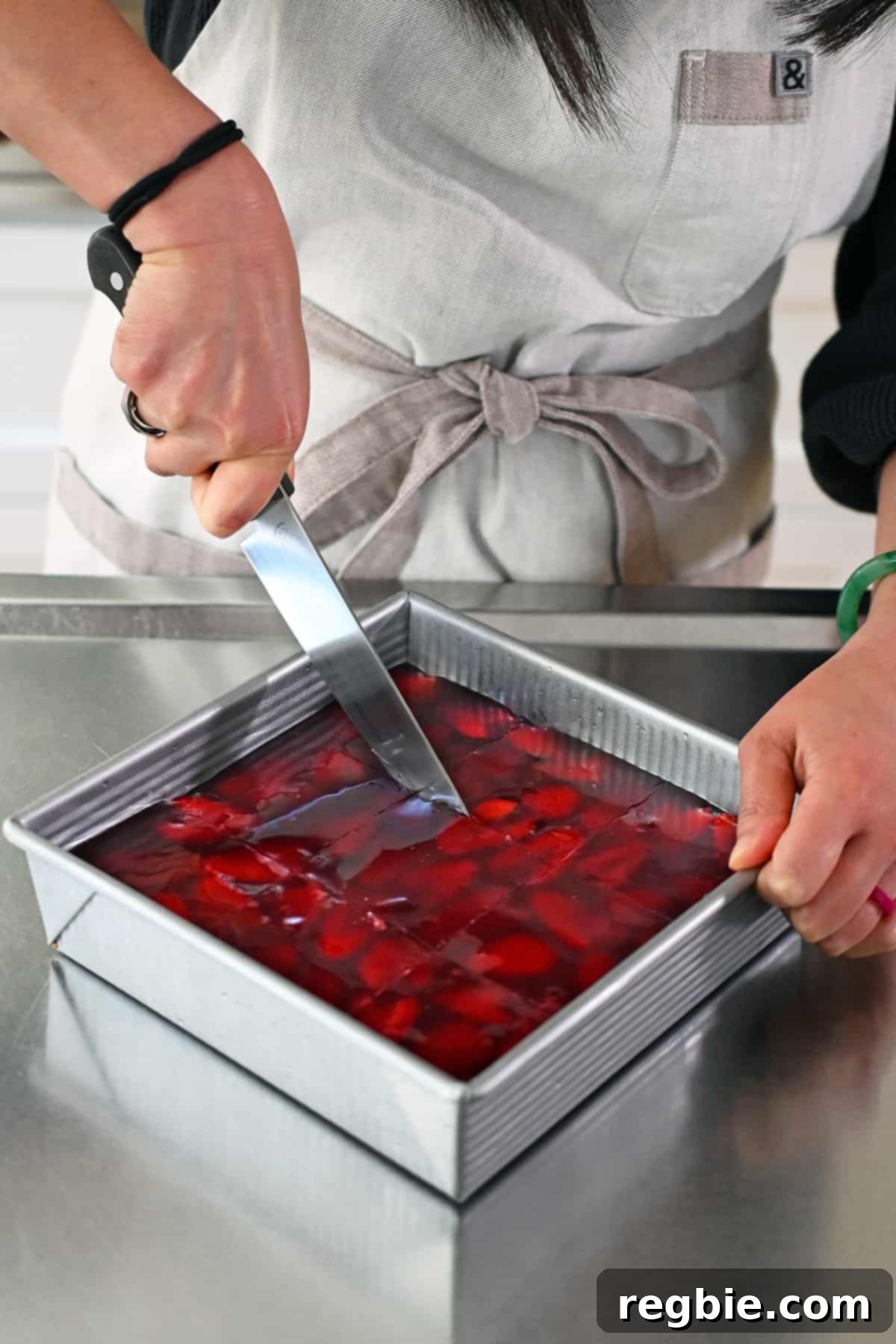 Slicing a strawberry pretzel salad into nine even squares, revealing the beautifully defined layers.