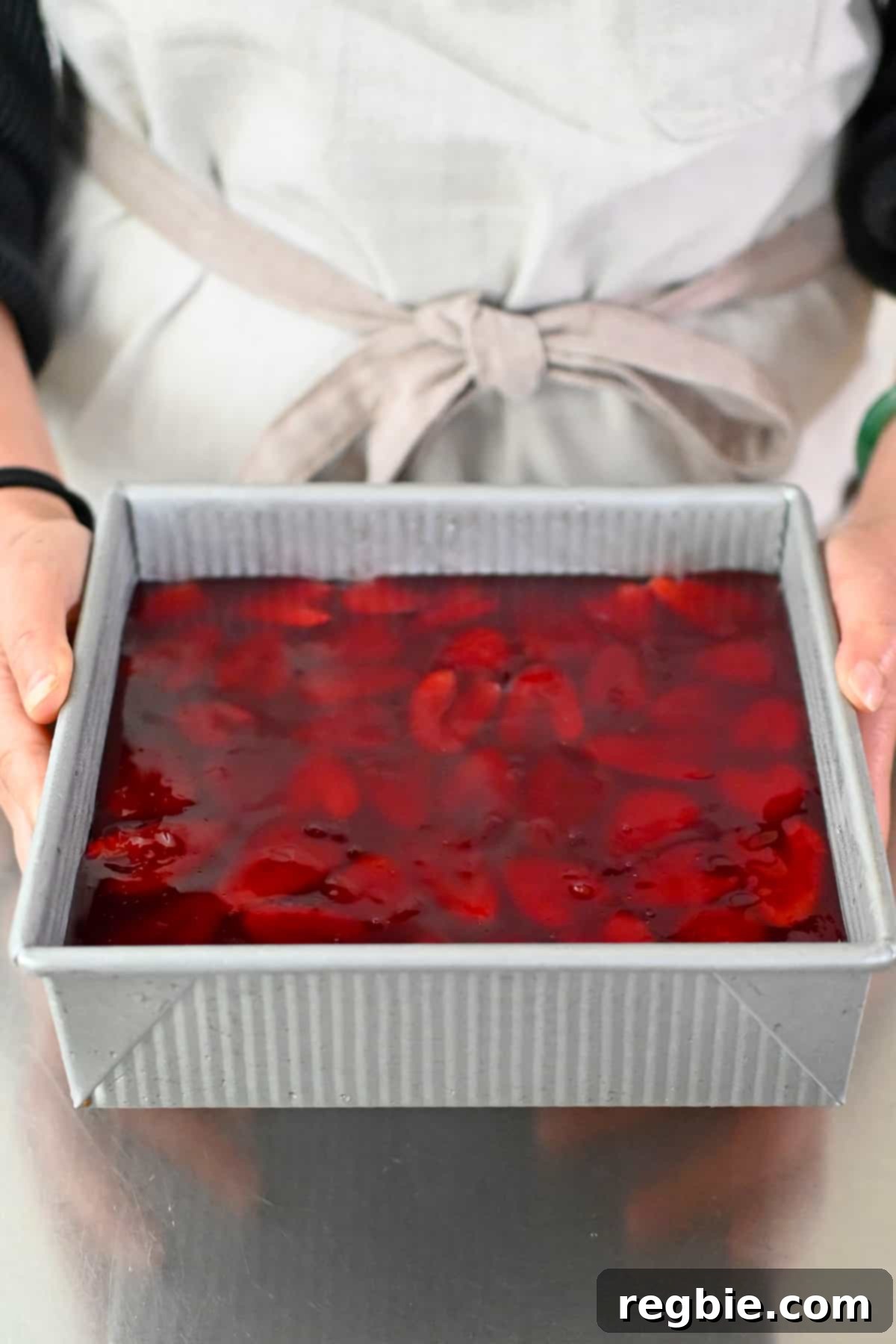 A person in a beige apron is holding a fully chilled grain-free and dairy-free strawberry pretzel salad, perfectly set and ready to be served.