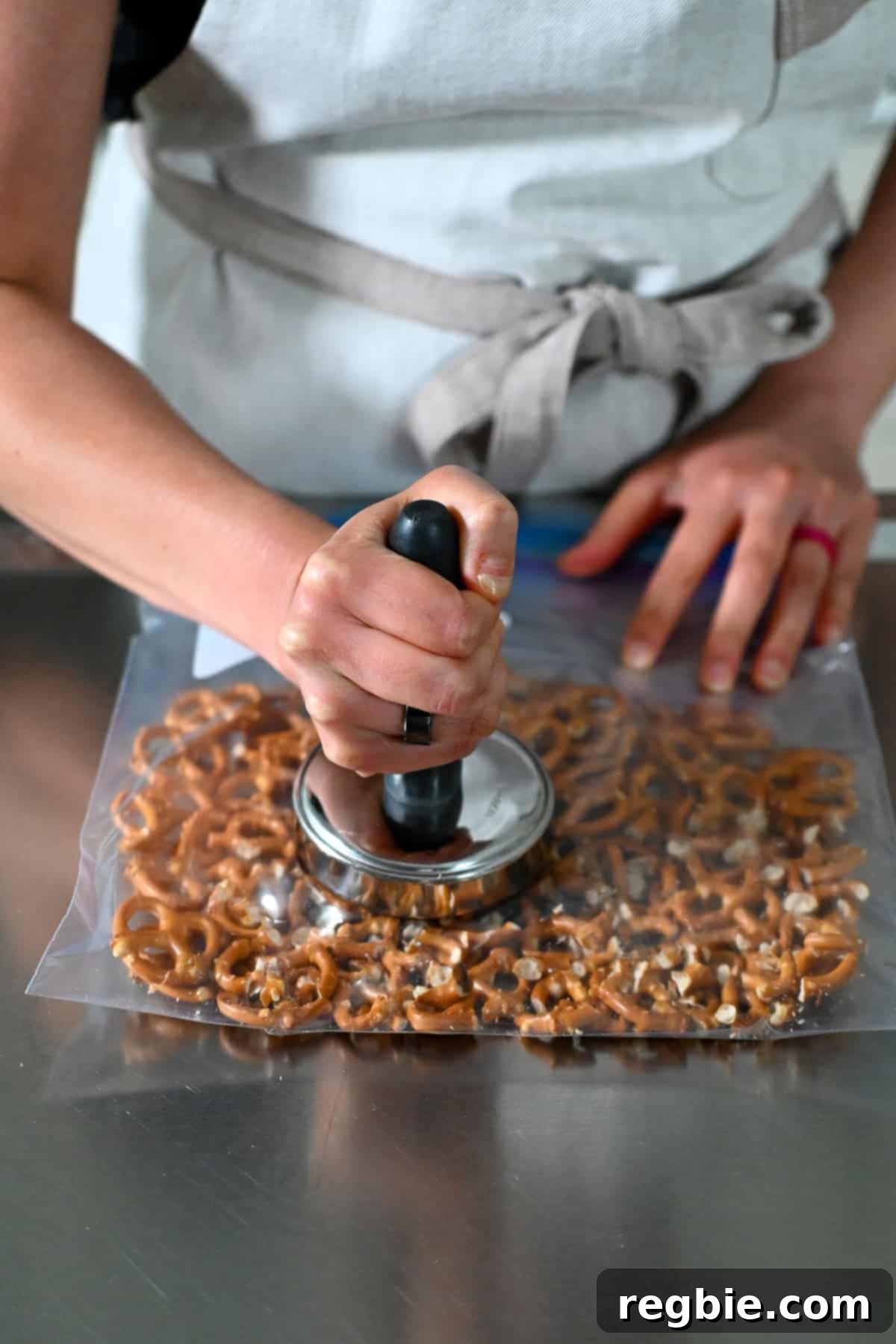 Crushing pretzels in a sealed plastic bag with a meat pounder for the strawberry pretzel salad crust, ensuring a good texture for the base.