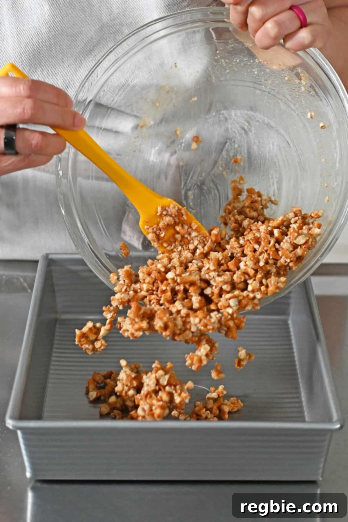 Transferring the prepared pretzel crust mixture to a square baking pan to form the base for the strawberry pretzel salad.
