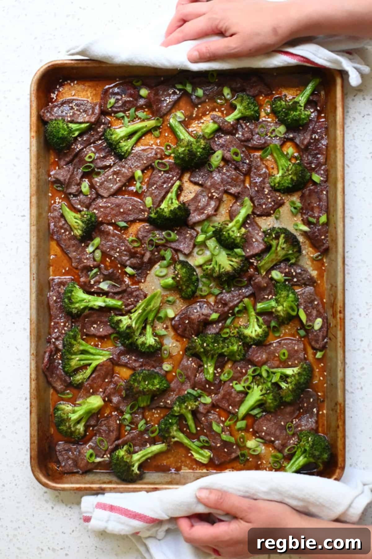 An overhead shot of perfectly cooked sheet pan broccoli and beef, generously topped with fresh sliced green onions and toasted sesame seeds, ready to be served.