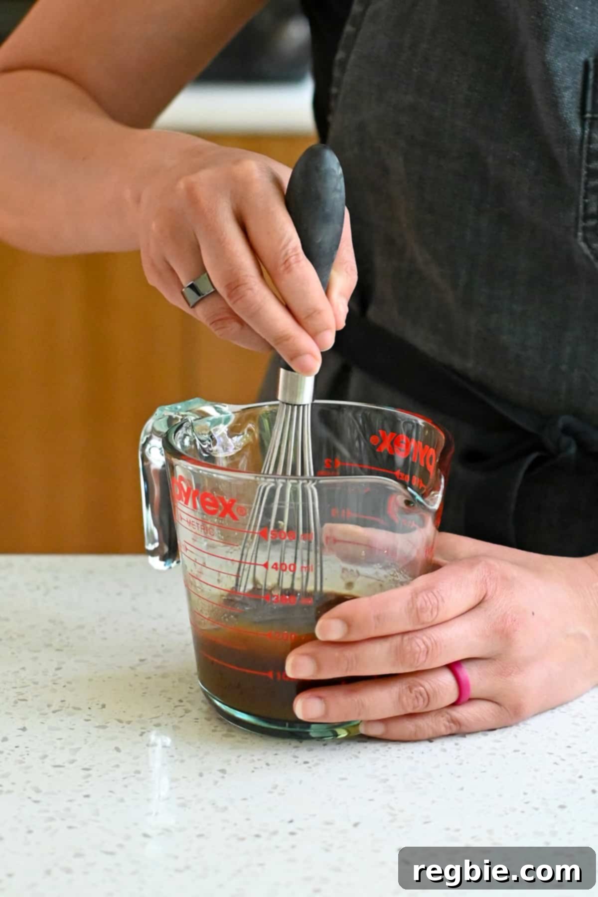 A hand whisking arrowroot powder into the All-Purpose Stir-Fry Sauce in a liquid measuring cup, creating a smooth mixture.