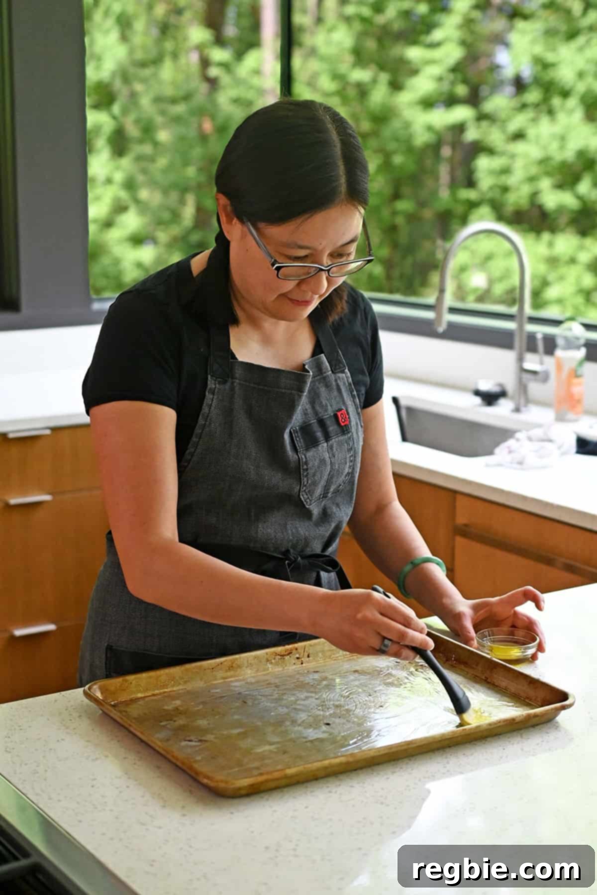 An Asian woman is carefully brushing a sheet pan with some avocado oil, preparing it for the ingredients.