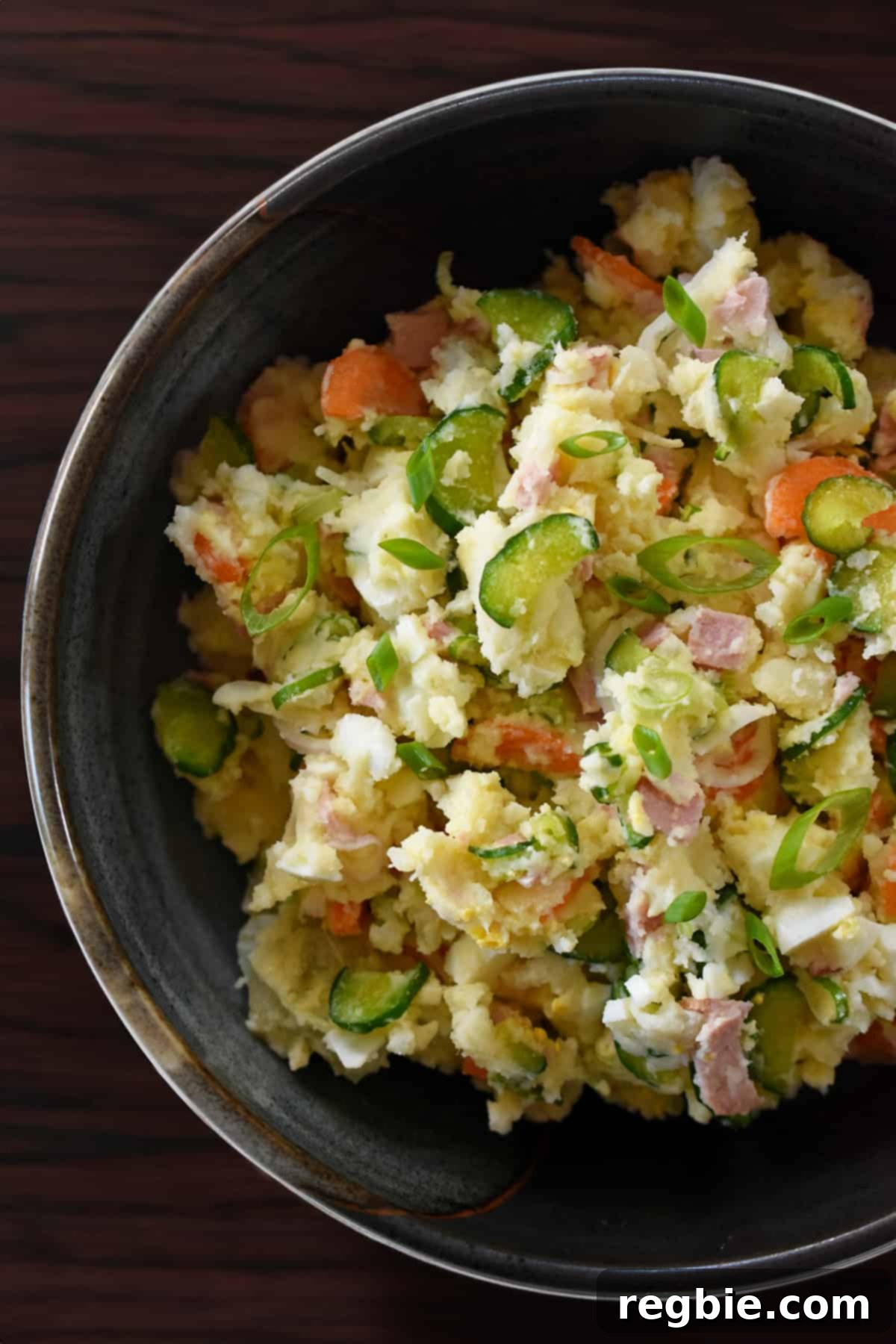 An overhead shot of a serving bowl filled with Japanese potato salad, highlighting its creamy texture and visible ingredients like carrots, cucumbers, and eggs.