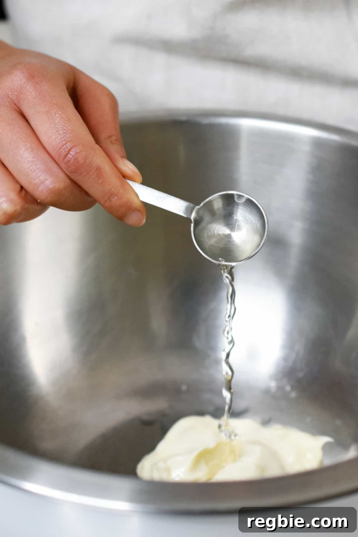 Adding a spoonful of rice vinegar into a mixing bowl with a dollop of mayonnaise, starting the dressing preparation.