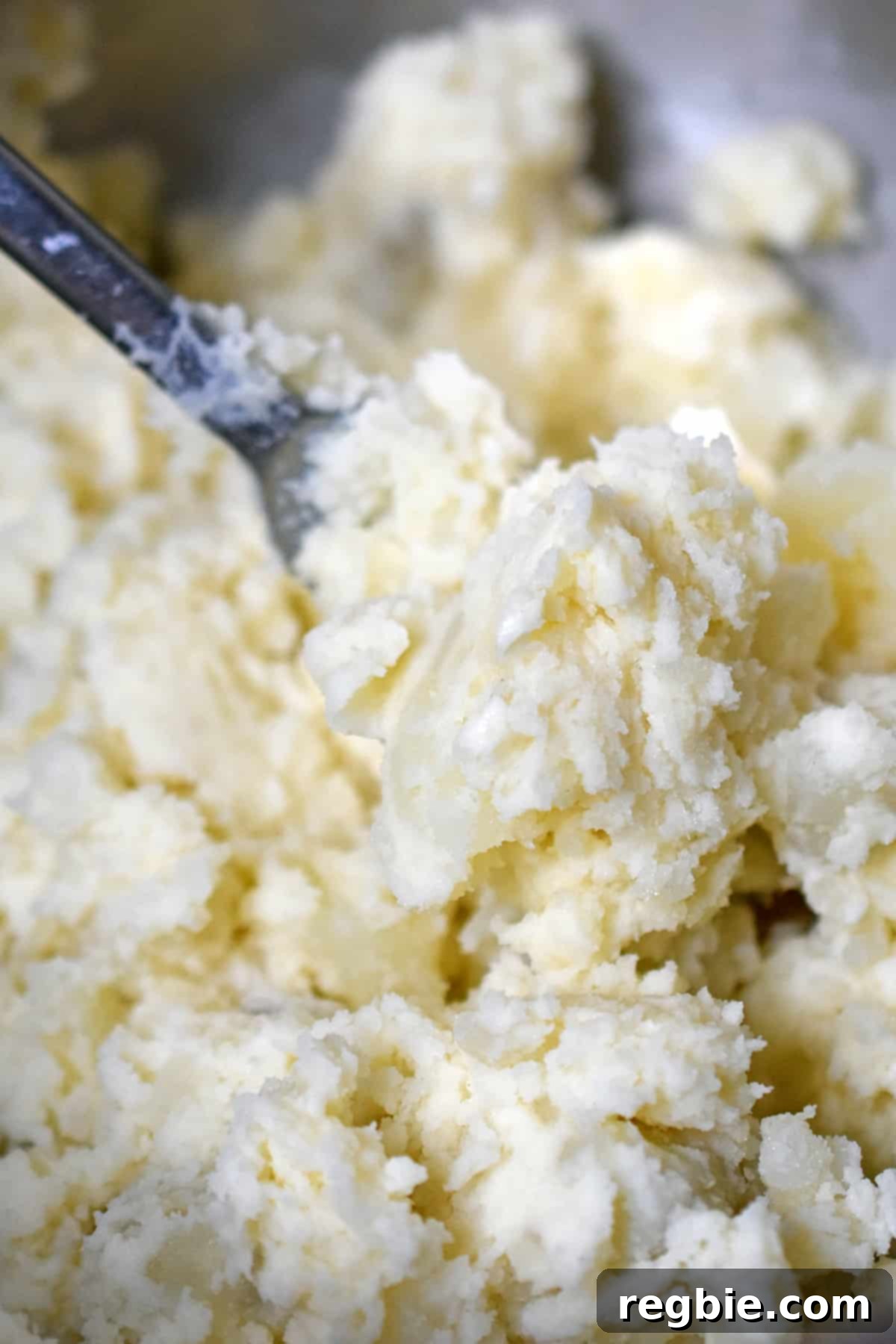 A closeup of mashed russet potatoes being combined with seasoned mayonnaise to create the creamy base of Japanese potato salad.