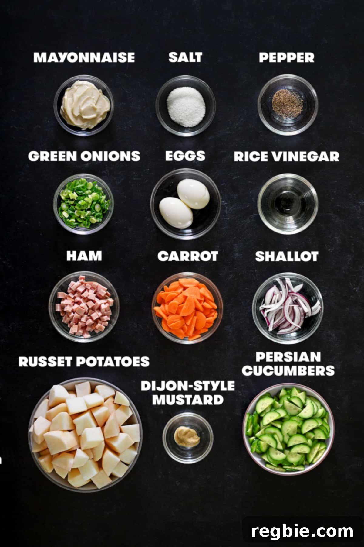 An overhead shot of the raw ingredients for Japanese potato salad neatly arranged on a counter, including potatoes, cucumbers, carrots, eggs, and mayonnaise.