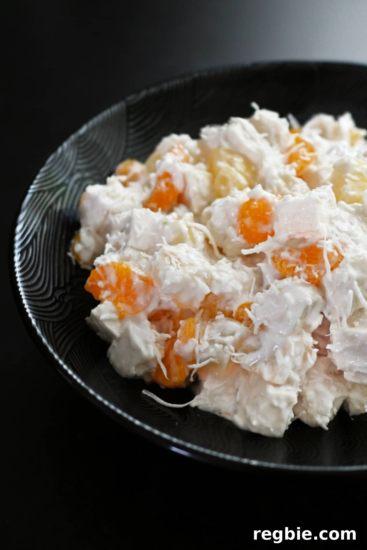 A closeup shot of a bowl of paleo ambrosia salad, highlighting its creamy texture and vibrant fruit pieces, ready to be enjoyed.