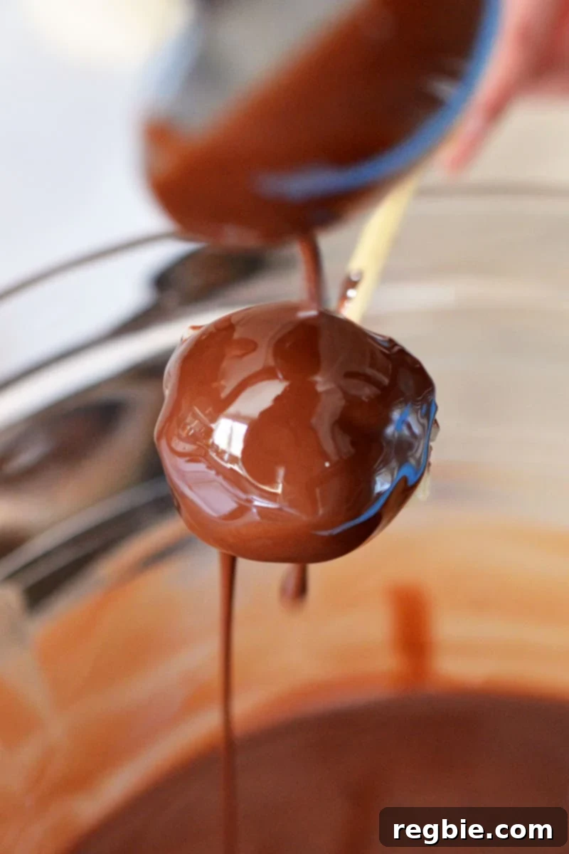 Guilt-Free Chunky Monkey Nice Cream Bonbons 15 A delicious small scoop of banana nice cream is being gracefully covered with rich melted chocolate using a spoon, a delightful step in crafting Chunky Monkey Ice Cream Bon Bons.