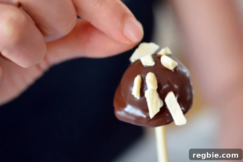 Guilt-Free Chunky Monkey Nice Cream Bonbons 16 A hand gently adds a sprinkle of toasted slivered almonds to a freshly chocolate-dipped Chunky Monkey Ice Cream Bon Bon, adding that essential crunch and flavor.
