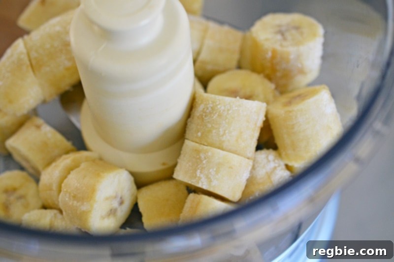 Guilt-Free Chunky Monkey Nice Cream Bonbons 5 An inviting overhead shot of perfectly frozen banana slices nestled in an open food processor, ready to be transformed into creamy nice cream.