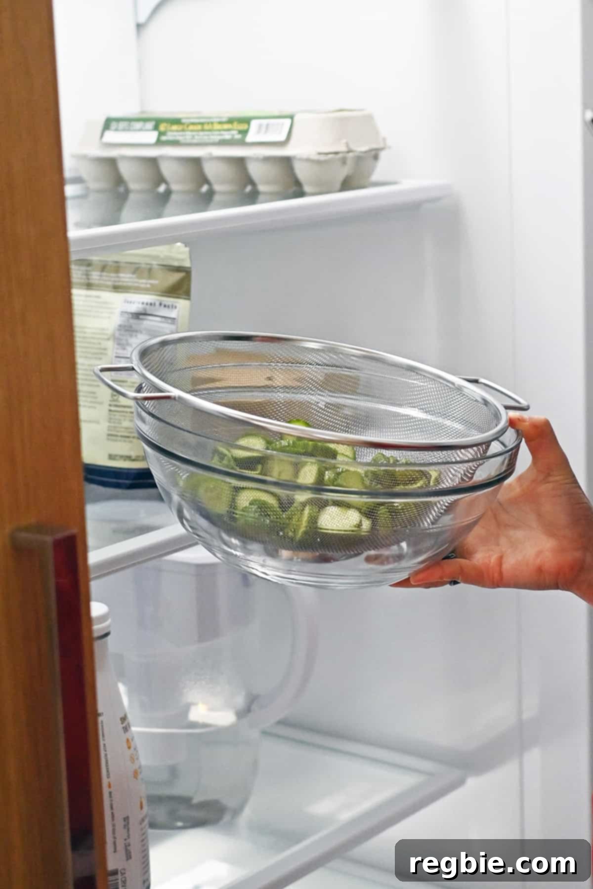 The process of placing salted cucumber slices in a colander, nested in a glass bowl, into the refrigerator to drain and crisp.