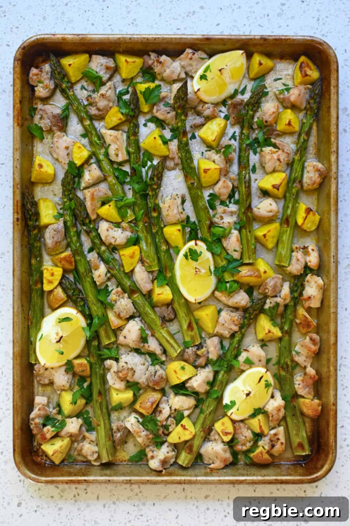 Zesty Mediterranean Sheet Pan Chicken 2 A beautifully arranged overhead shot of golden-brown Greek sheet pan chicken, perfectly roasted asparagus, and crispy potatoes, garnished with fresh Italian parsley and lemon wedges.