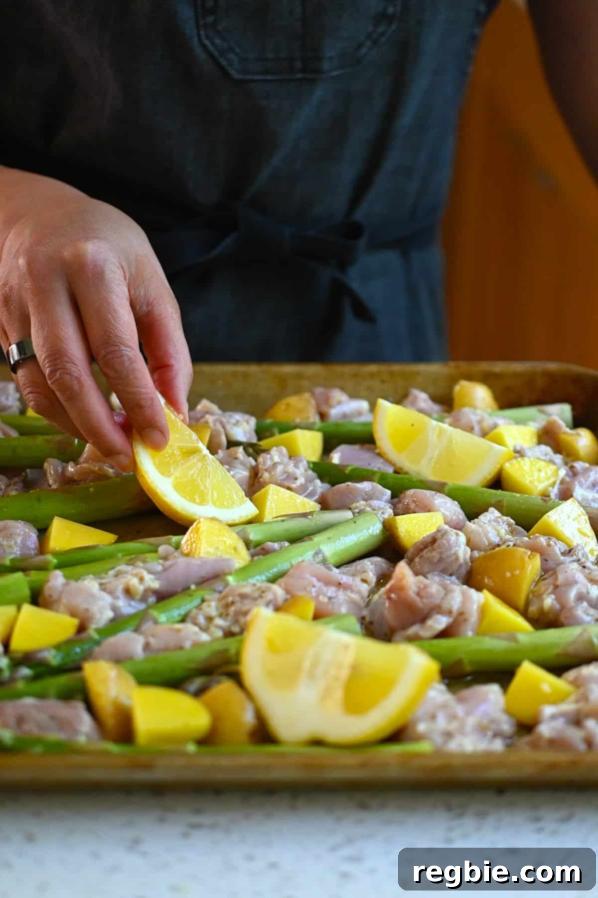 Zesty Mediterranean Sheet Pan Chicken 12 Lemon wedges are carefully added to the sheet pan, nestled among the seasoned chicken, asparagus, and potatoes, enhancing the Greek flavor profile and preparing for roasting.