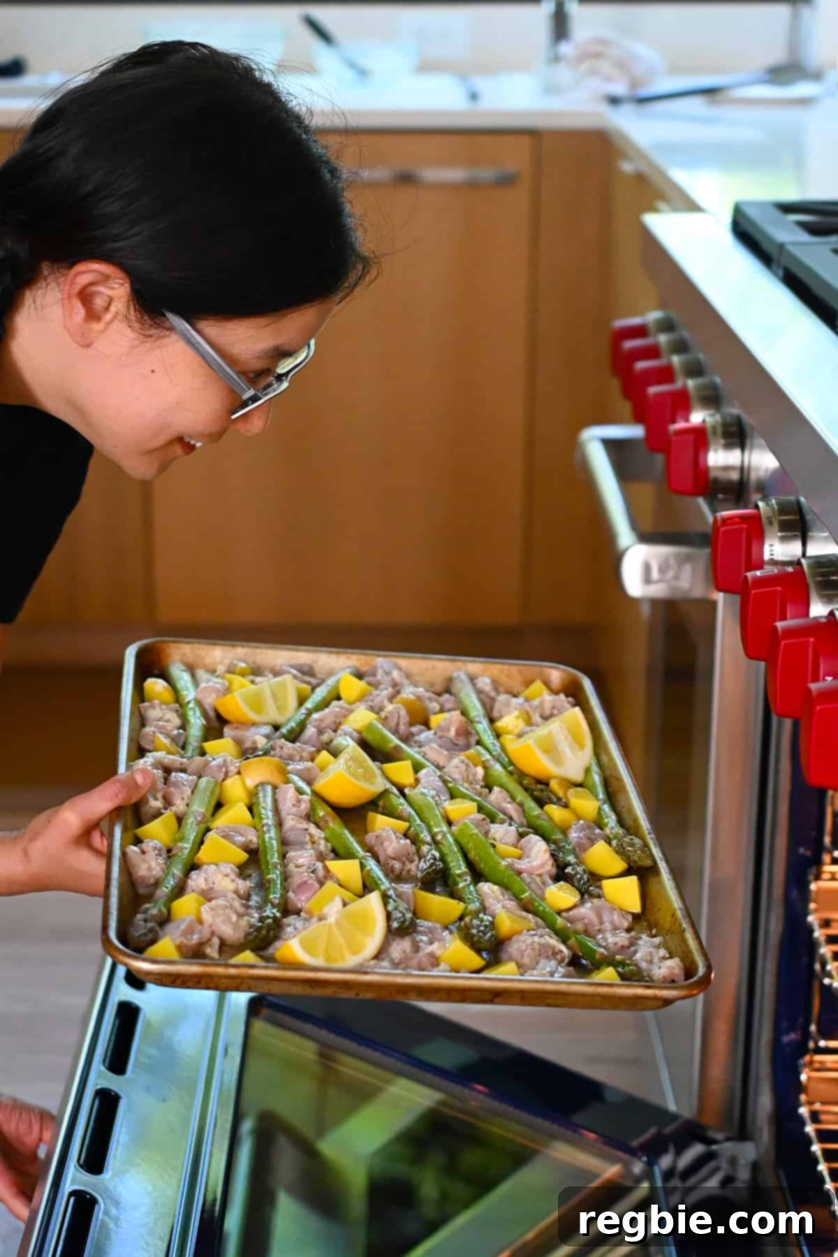 Zesty Mediterranean Sheet Pan Chicken 13 An Asian woman carefully slides a prepared Greek sheet pan chicken dinner into an open, preheated oven, ready to begin its transformation.