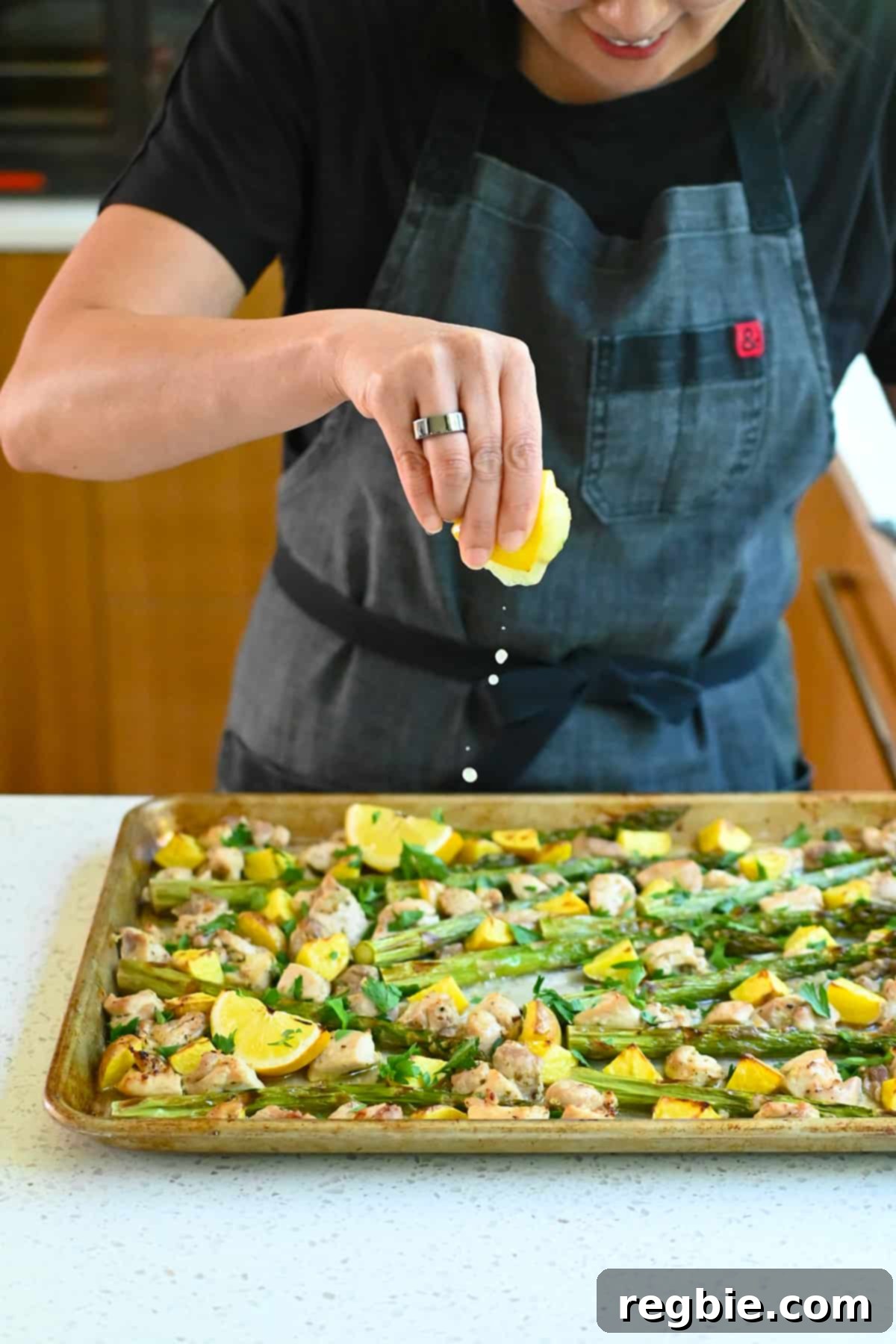 Zesty Mediterranean Sheet Pan Chicken 16 A hand gently squeezes fresh, charred lemon juice directly onto the vibrant Greek Sheet Pan Chicken dinner, infusing it with a final burst of zesty flavor before serving.