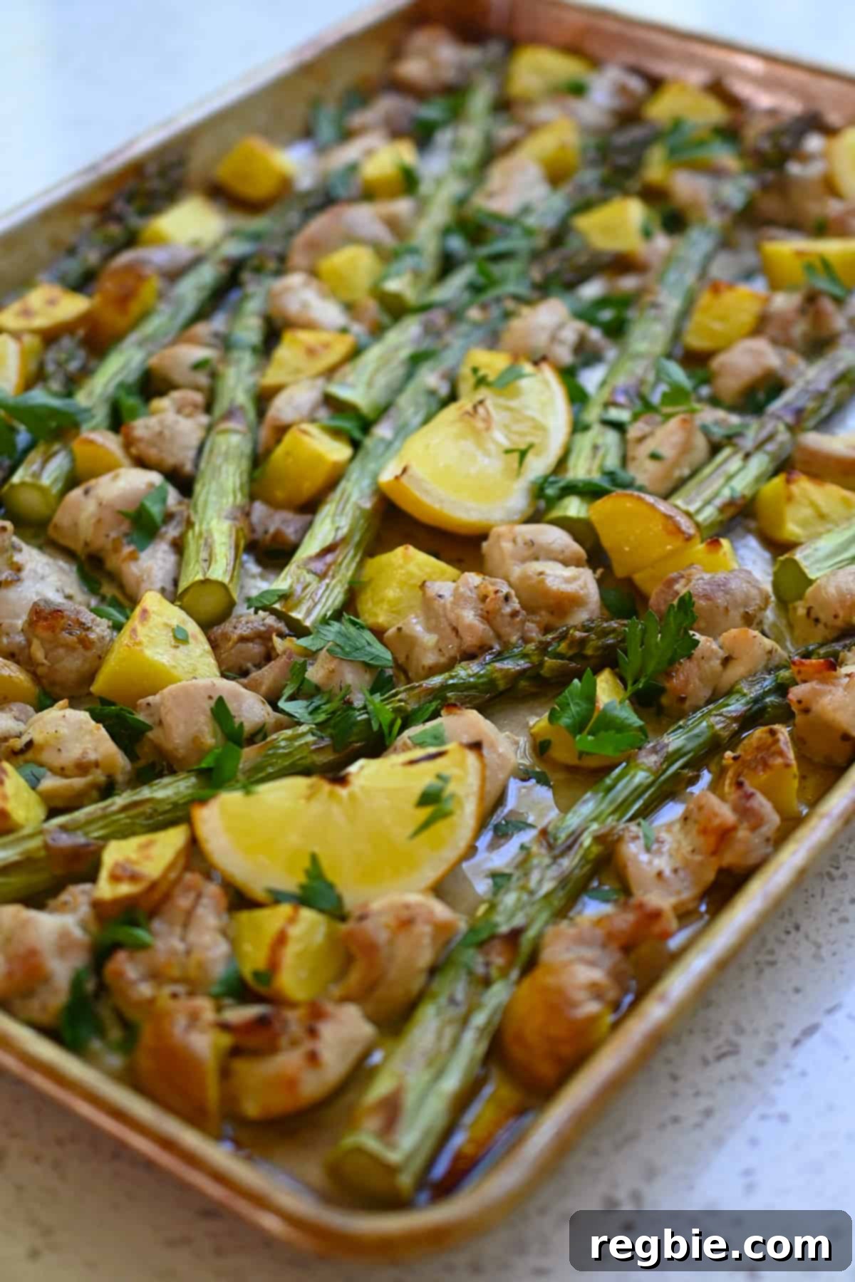 Zesty Mediterranean Sheet Pan Chicken 3 A tantalizing side view of a Greek sheet pan chicken dinner, showcasing perfectly cooked asparagus, golden potatoes, tender chicken pieces, and charred lemon wedges, ready to be enjoyed.