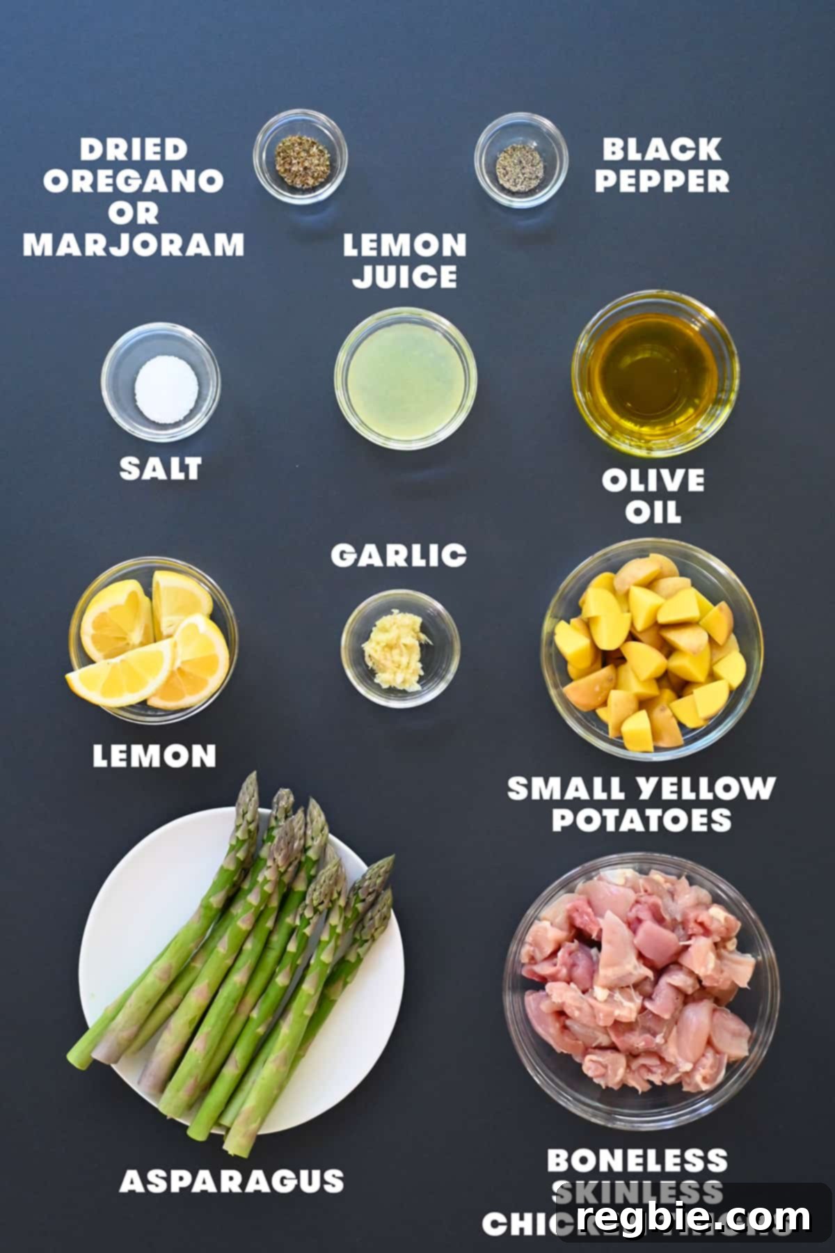 Zesty Mediterranean Sheet Pan Chicken 4 A vibrant collection of fresh ingredients laid out on a kitchen counter: boneless chicken thighs, small yellow potatoes, bright green asparagus spears, whole lemons, garlic cloves, and a small bowl of dried oregano.