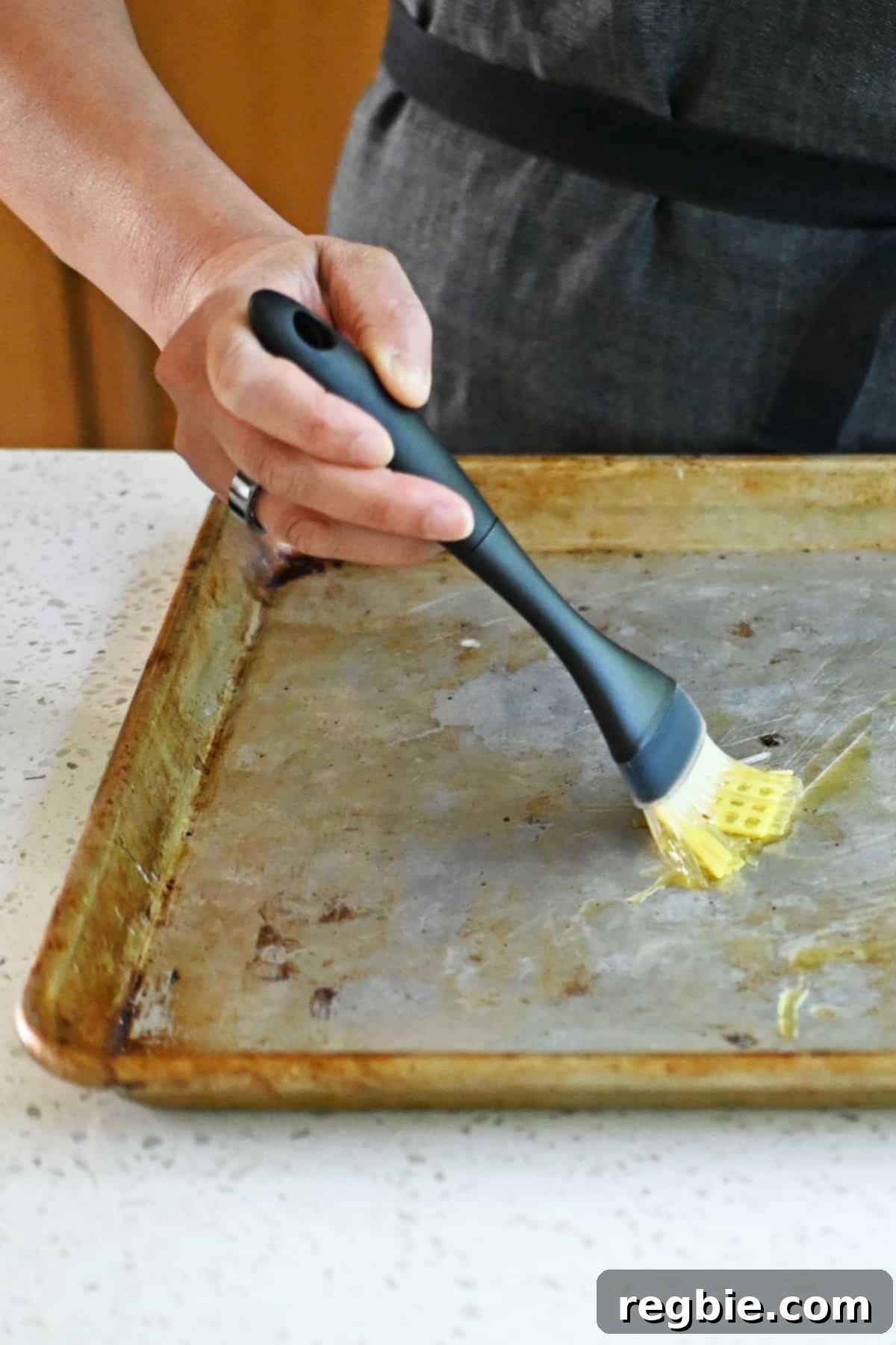 Zesty Mediterranean Sheet Pan Chicken 5 A silicone brush expertly spreads a thin, even layer of extra virgin olive oil across a rimmed baking sheet, preparing it for a delicious sheet pan meal.