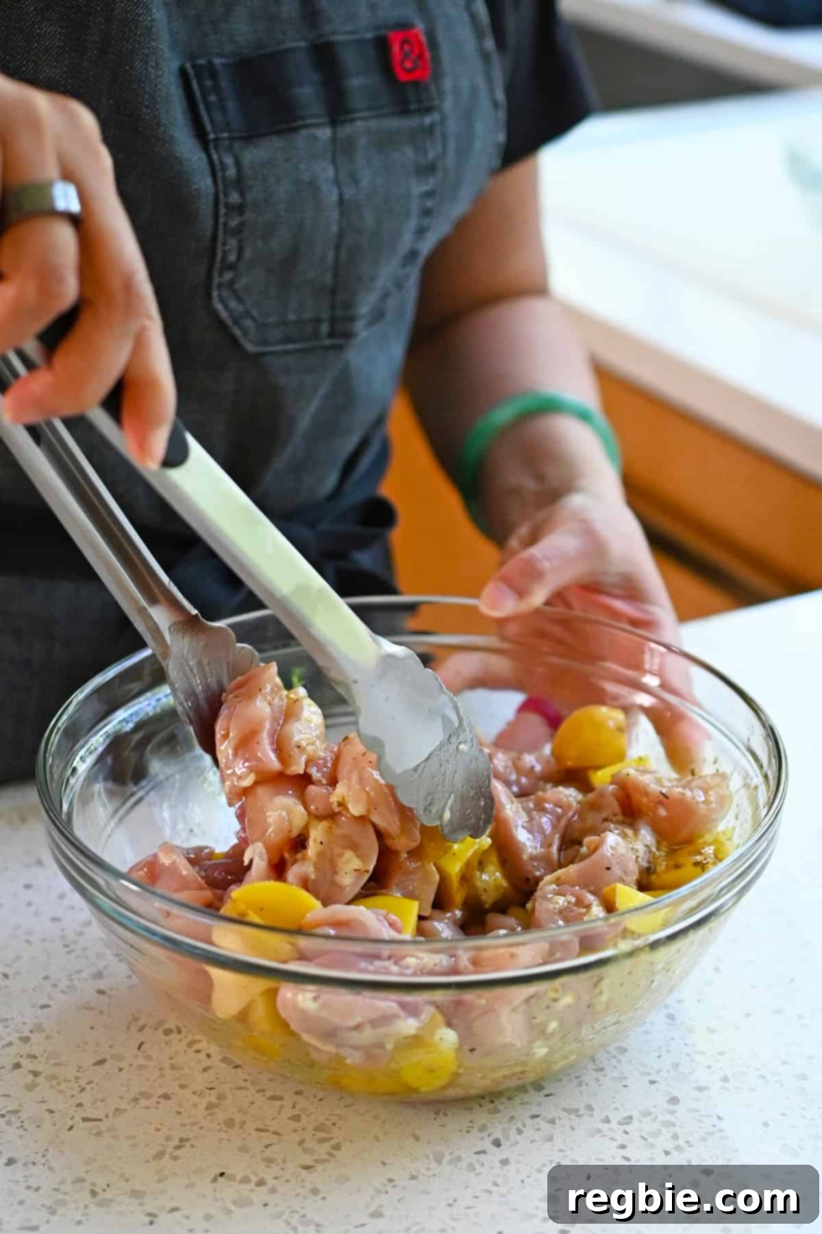 Zesty Mediterranean Sheet Pan Chicken 9 Hands expertly tossing raw chicken thigh cubes and uniformly cut yellow potatoes in a bowl, ensuring a thorough coating with the vibrant Greek marinade for maximum flavor infusion.