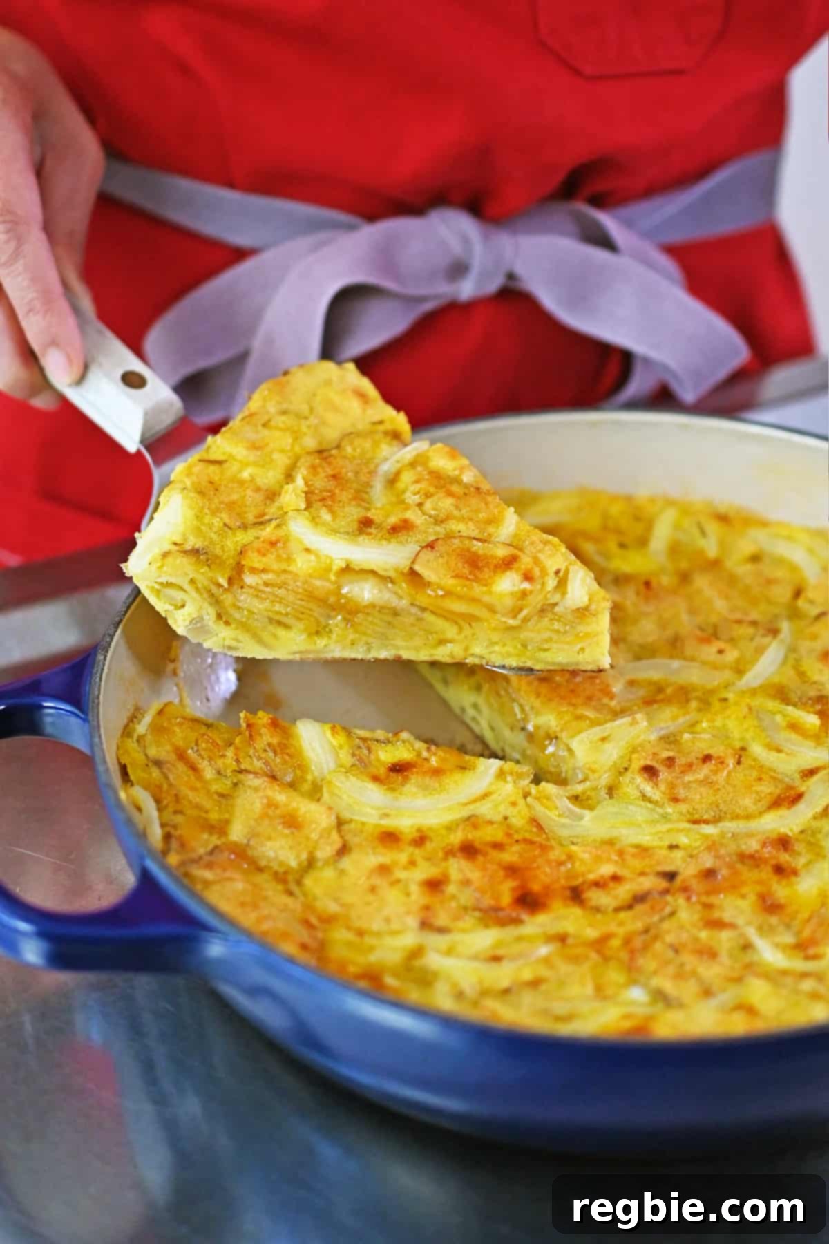 Crispy Potato Chip Tortilla 2 Lifting up a slice of Spanish tortilla made with potato chips from a blue skillet.