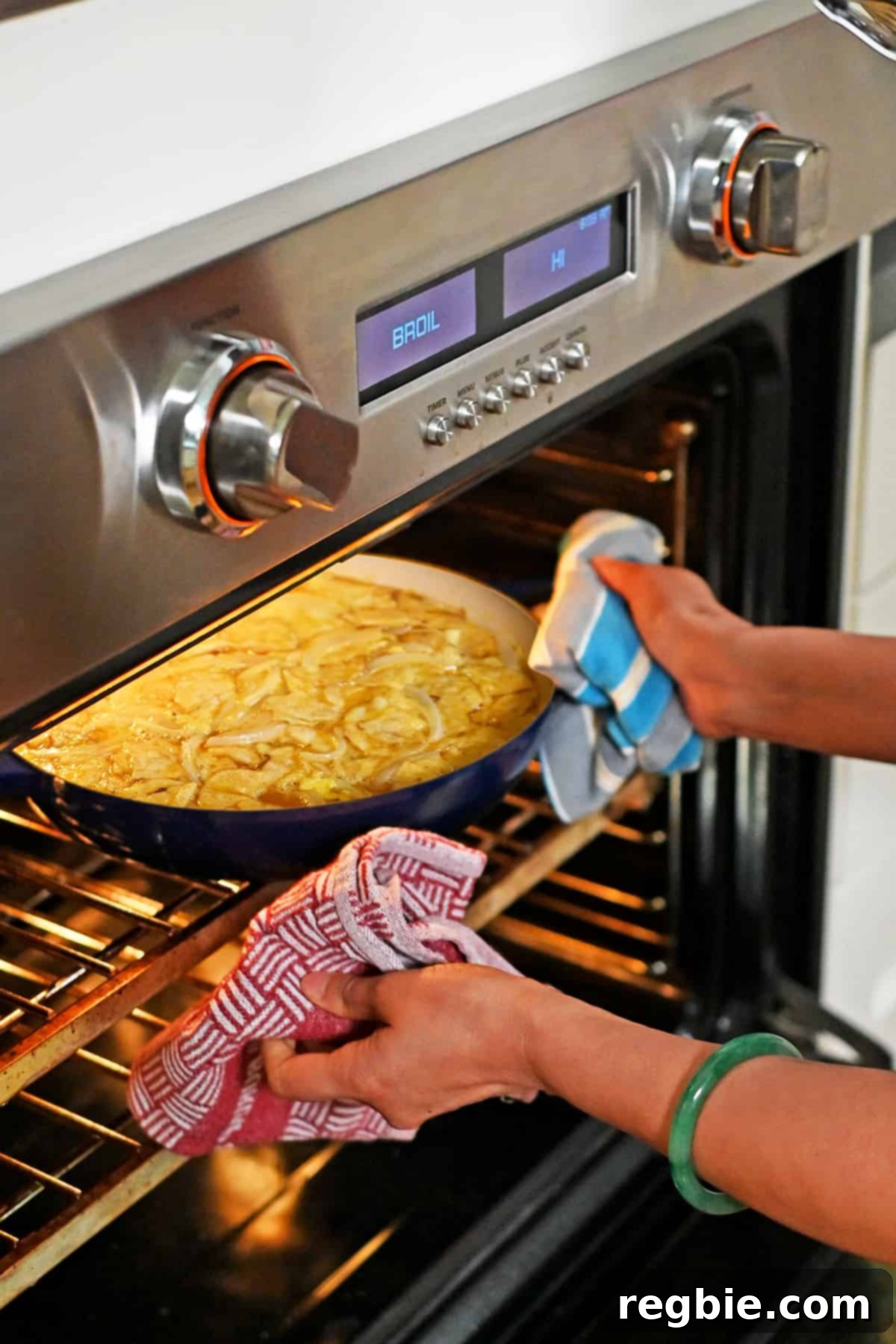 Crispy Potato Chip Tortilla 14 Two hands are placing a blue skillet filled with Spanish tortilla made with potato chips into an oven set on broil.