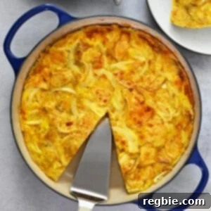 An overhead shot of a skillet filled with a Spanish tortilla made with potato chips with a missing slice that is on a plate next to the pan.