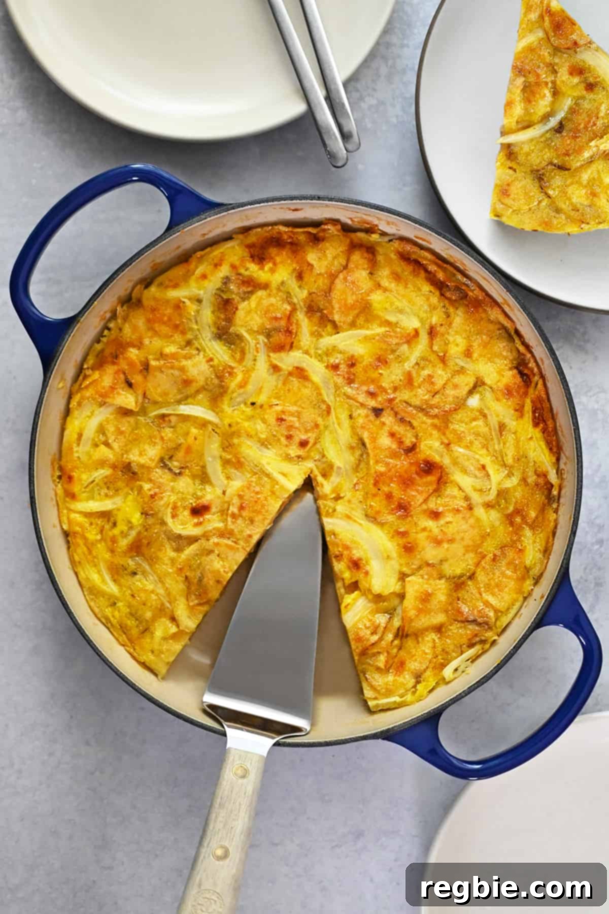 Crispy Potato Chip Tortilla 3 An overhead shot of a skillet filled with a Spanish tortilla made with potato chips with a missing slice that is on a plate next to the pan.