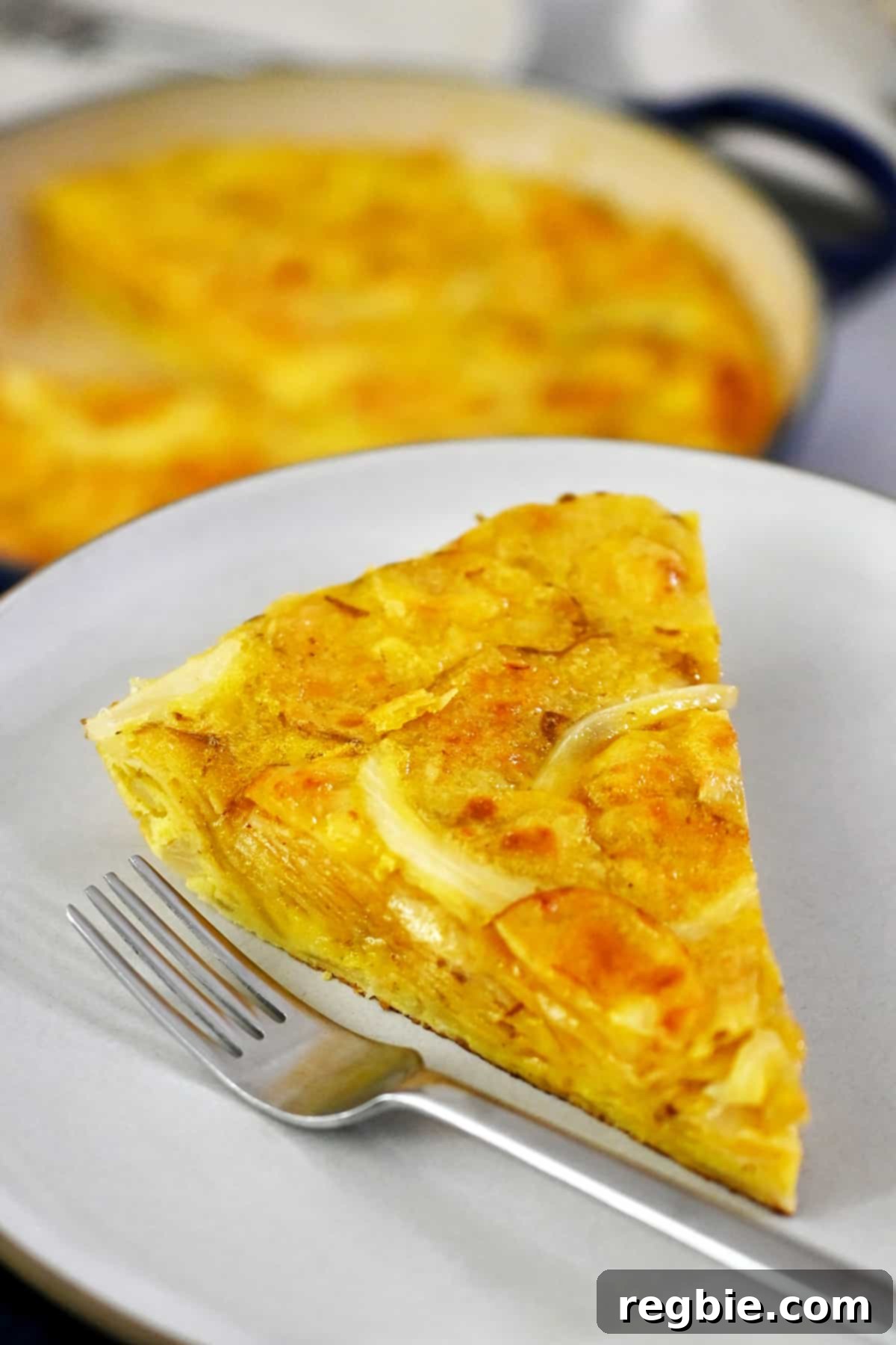 Crispy Potato Chip Tortilla 4 A slice of Spanish tortilla made with potato chips on a white plate next to a fork.