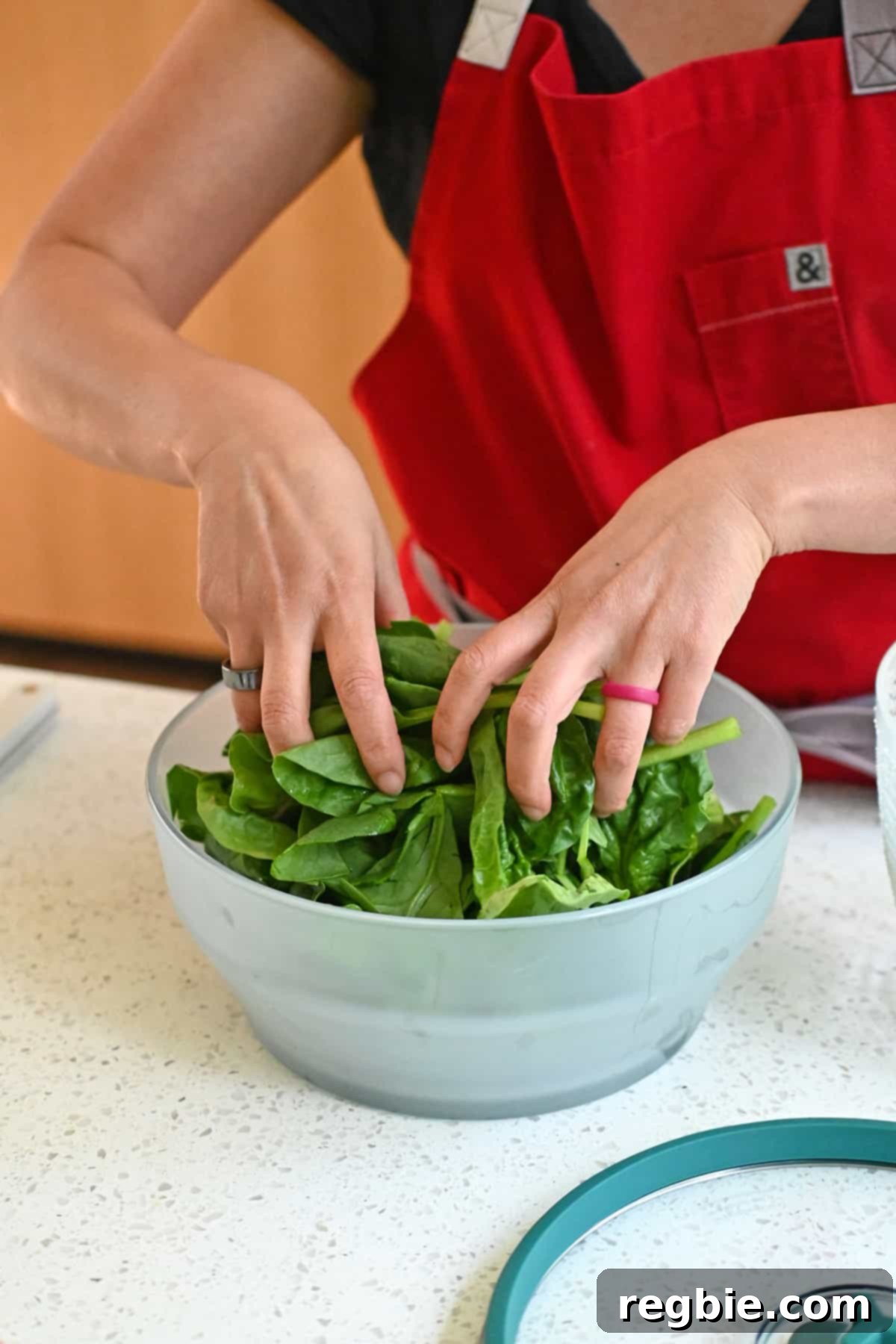 A close-up shot of raw spinach being carefully placed into an extra-large, clear glass Anyday microwave container, ready for cooking.