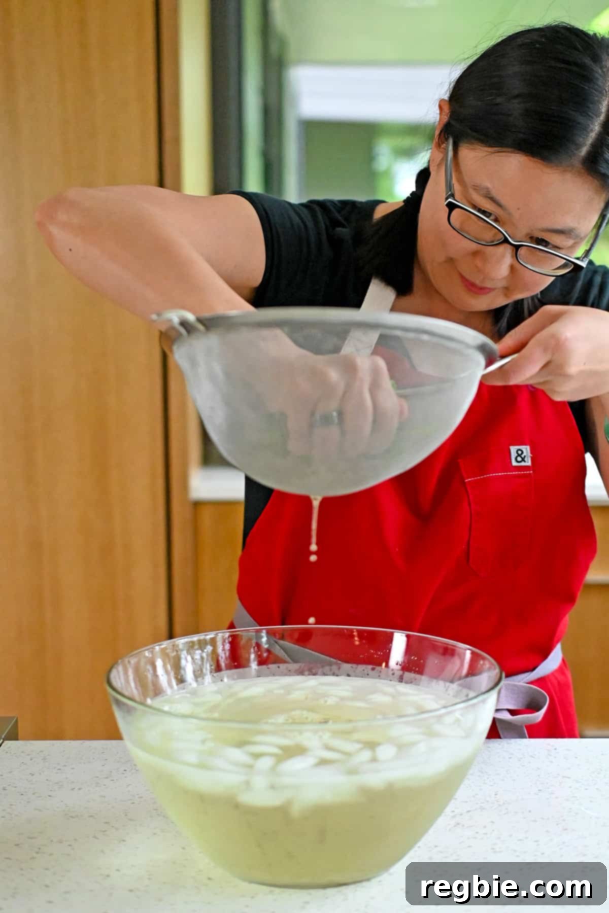 An Asian woman uses her hands to firmly squeeze excess water out of cooked and chilled spinach, preparing it for seasoning.