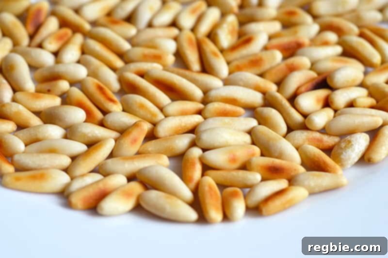 A small pile of perfectly golden-brown toasted pine nuts rests on a white plate, cooling after being removed from the heat.