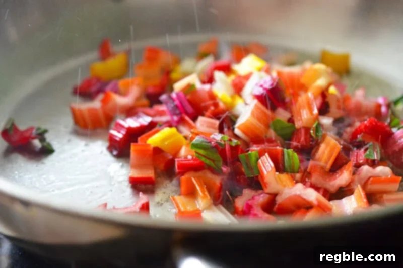 Vibrant rainbow chard stems are sizzling and sautéing in a hot pan with melted ghee, beginning to soften and develop flavor.