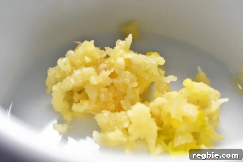 Freshly minced garlic cloves are neatly gathered in a small white bowl, ready to be added to the hot pan.