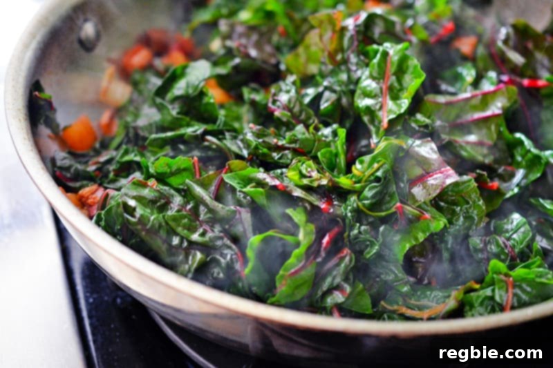 The Swiss chard leaves are actively wilting and cooking down in the pan, significantly reducing in volume as they soften and release moisture.