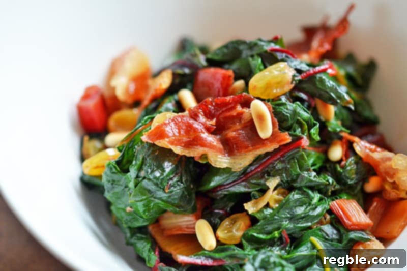 The finished Swiss Chard salad, beautifully garnished with golden raisins, toasted pine nuts, and crumbled crispy prosciutto, presented in a large serving bowl.