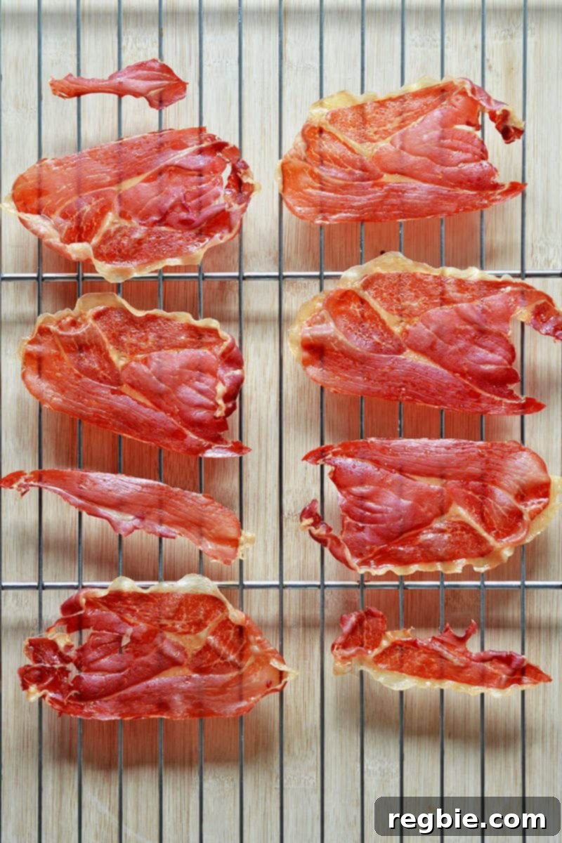 Several slices of crispy, golden-brown prosciutto laid out on a wire rack, cooling after being baked to perfection.