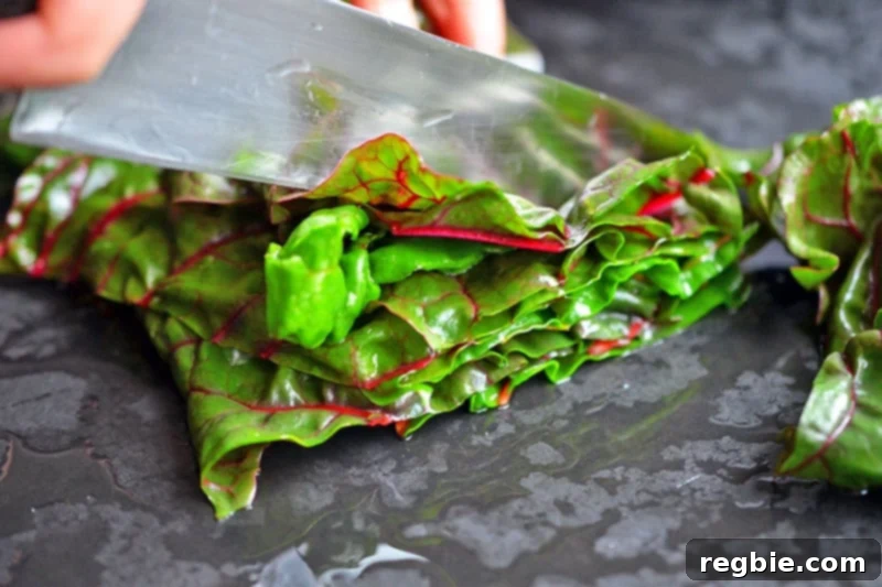 Neatly chopped Swiss chard leaves, cut into thick ribbons, are arranged on a cutting board, ready for the next cooking step.