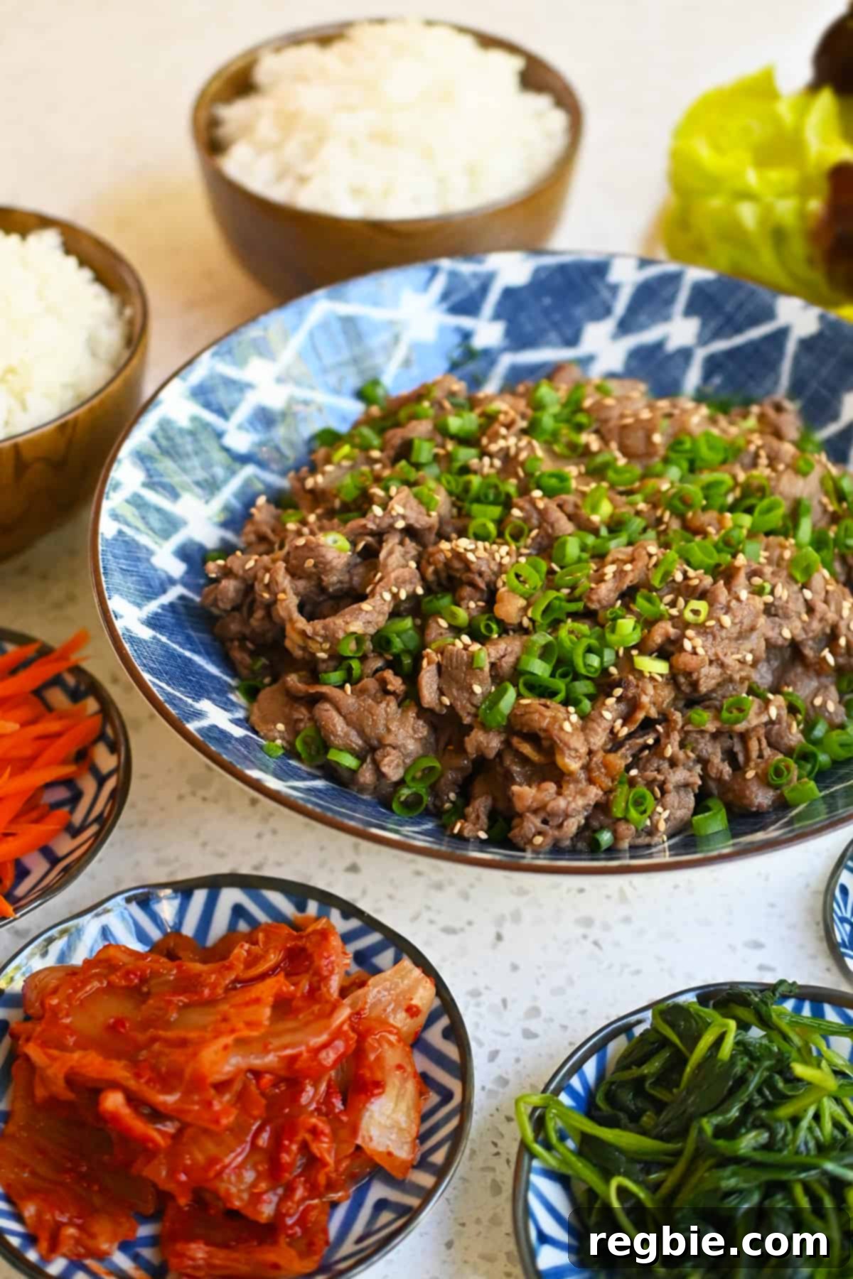A bowl of paleo and gluten free bulgogi surrounded by small bowls of banchan and steamed white rice.
