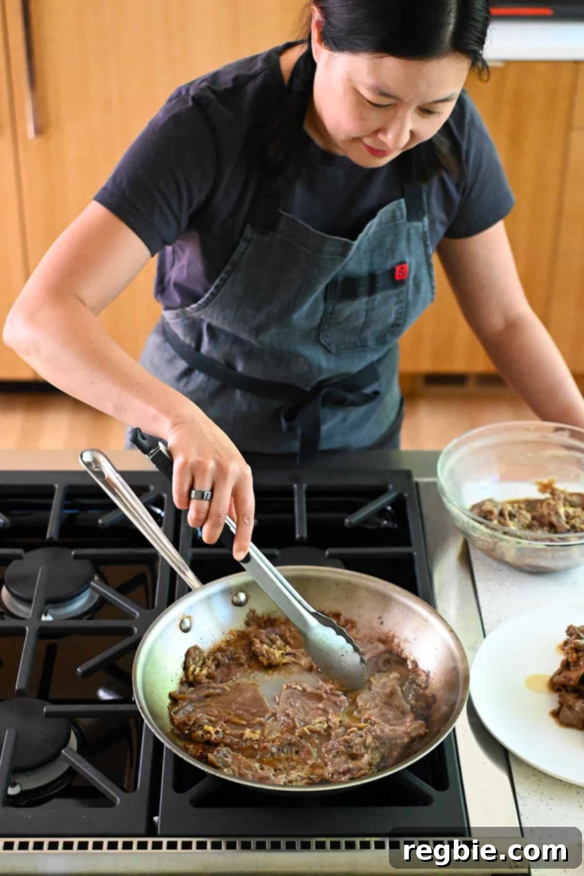 An Asian woman is cooking paleo bulgogi in a skillet on the stovetop in batches.