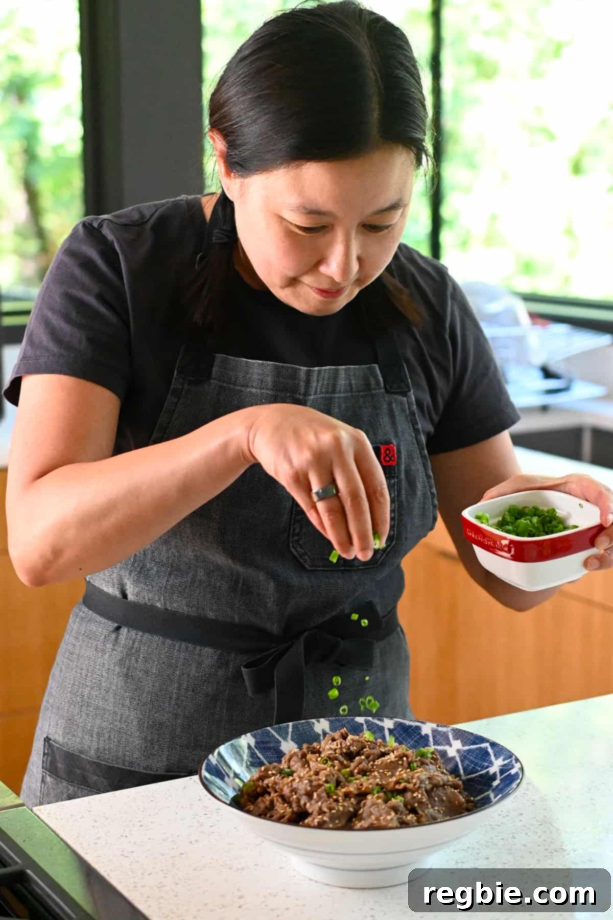 An Asian woman is sprinkling sliced green onions on a bowl of paleo and gluten free bulgogi.