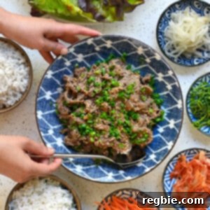 A hand is placing a serving spoon into a bowl of paleo bulgogi. There are small bowls of vegetables and steamed rice surrounding the beef.