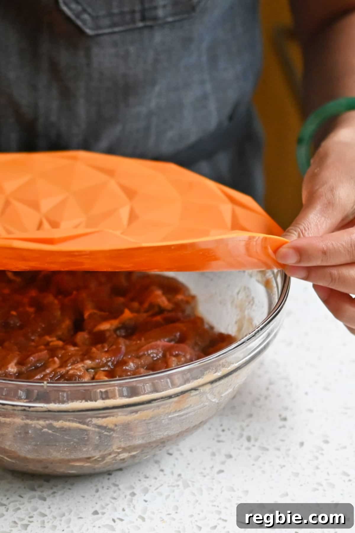 Placing an orange silicone lid on top of a bowl filled with marinated bulgogi beef.