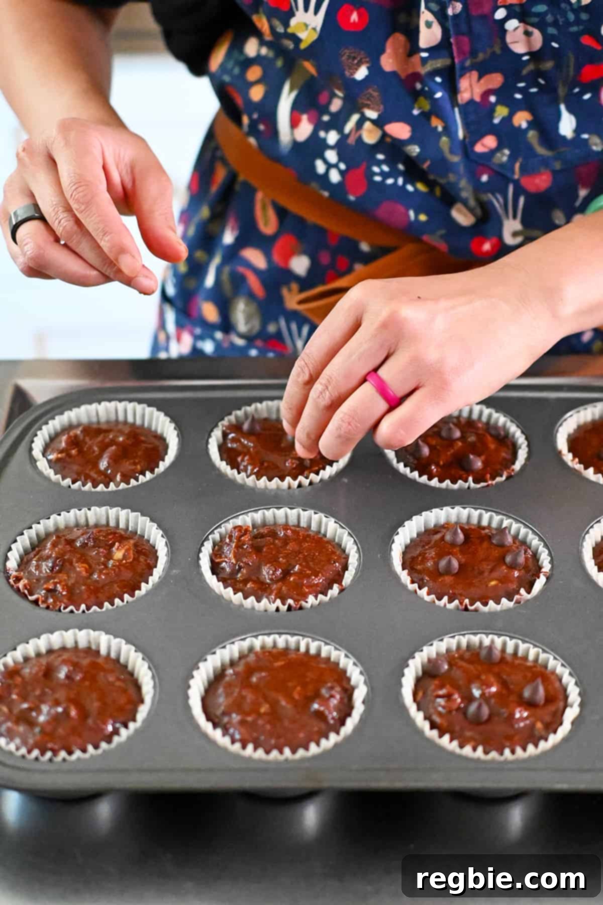 Adding extra chocolate chips on top of chocolate zucchini muffins before baking them in the oven, for an appealing finish.