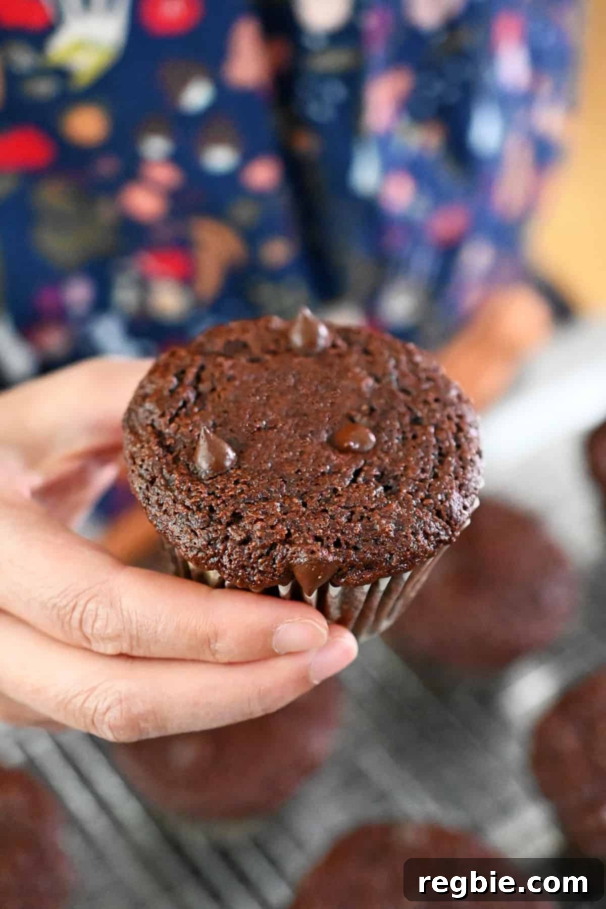A hand is holding a paleo and gluten-free chocolate zucchini muffin, showing its crumb and chocolate chips.
