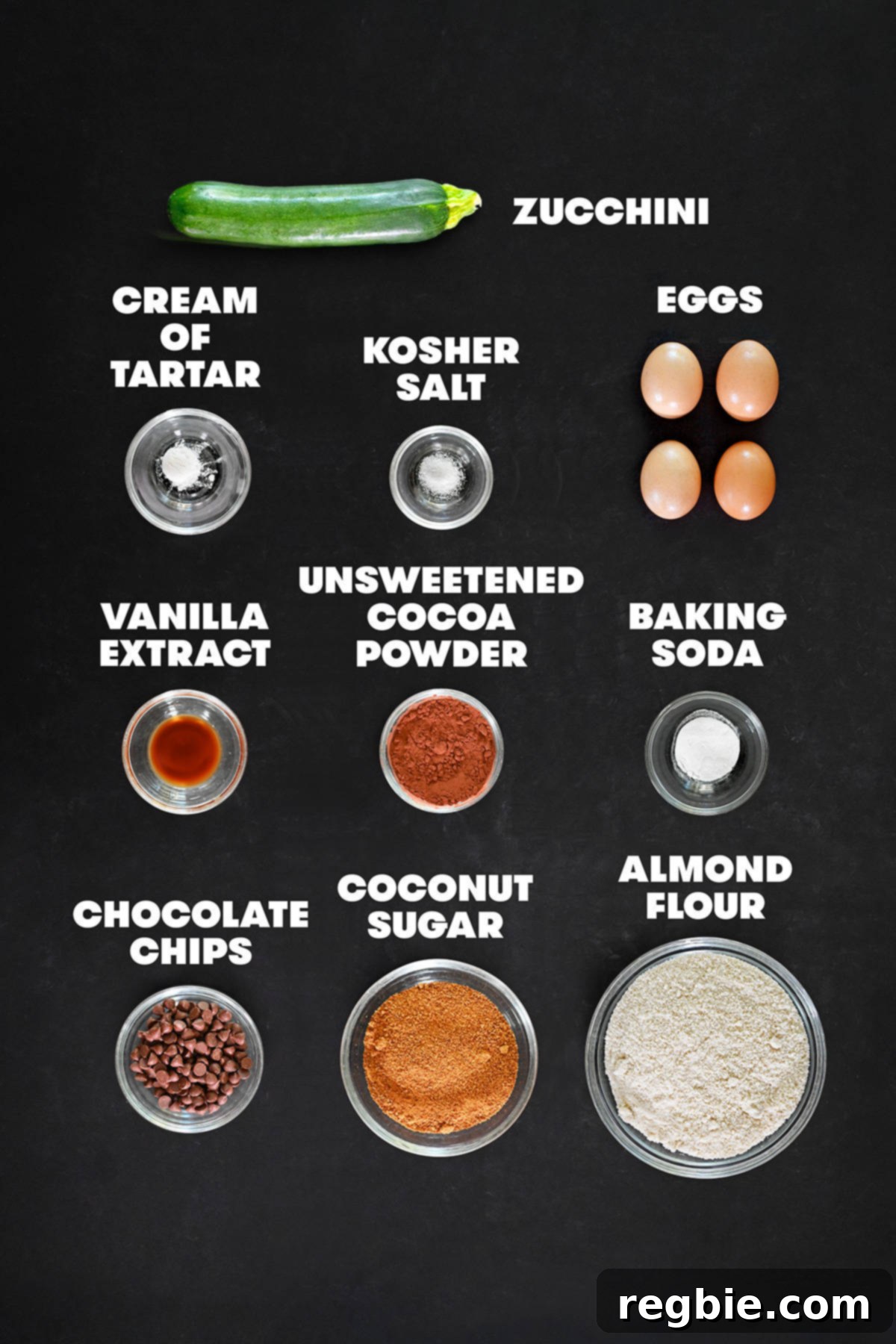 The raw ingredients measured out in bowls for paleo chocolate zucchini muffins, including zucchini, almond flour, cocoa powder, eggs, and chocolate chips.