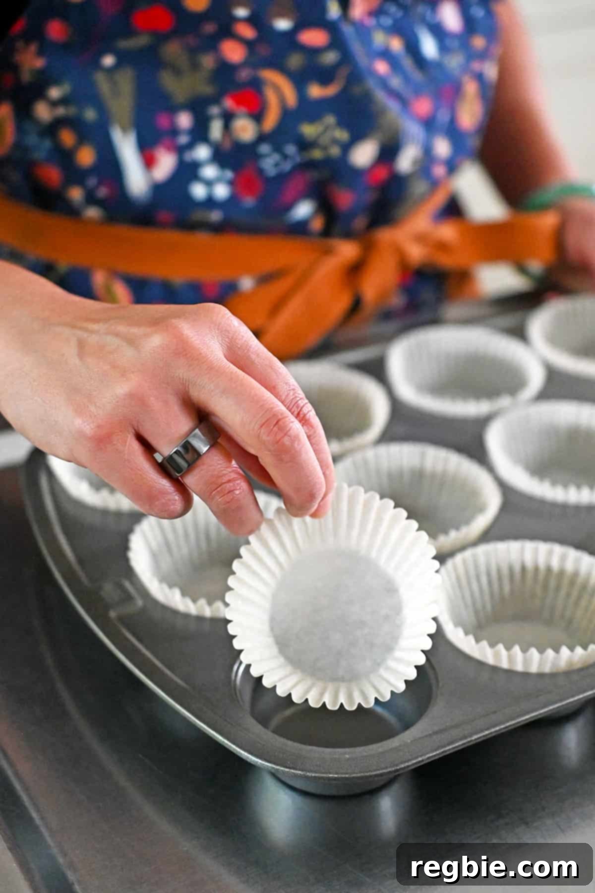 A hand is placing a parchment muffin liner into a muffin tin, preparing it for batter.