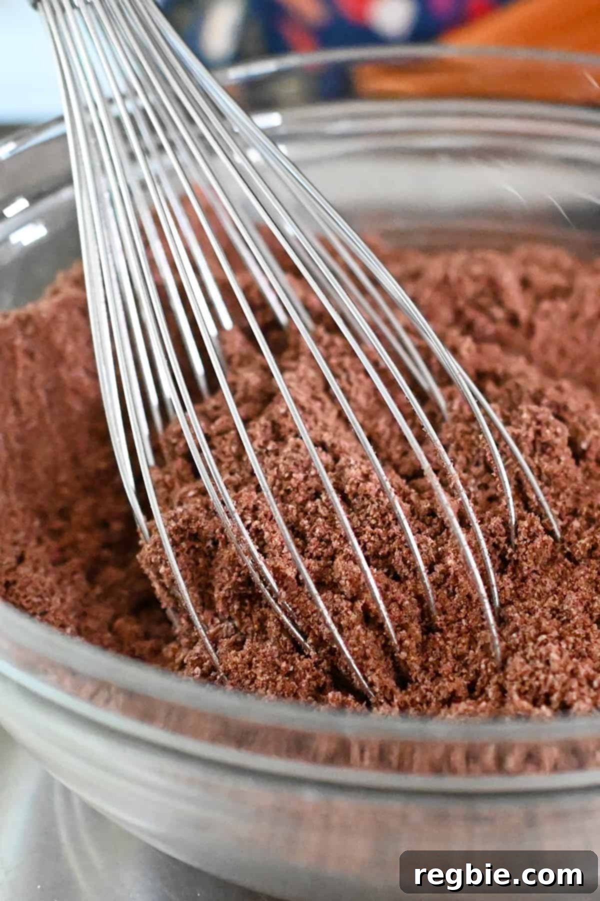 A metal whisk is stirring the dry ingredients in a bowl for chocolate zucchini muffins, ensuring they are well-combined.